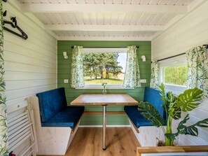 A compact room with a green wall, a window with curtains, a table, and two blue cushioned seats. - De Glamping - Trio Tiny Houses & Safaritent | 14p by Interhome (Zeewolde)