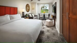 Quarto de hotel com uma cama grande, área de estar com mesa e cadeiras, televisão e vista para o exterior.