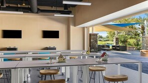 Un espacio exterior moderno para comer con varias mesas y sillas, un muro de piedra y vistas a un jardín ajardinado.
