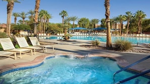 Un área de piscina con sillones de descanso, palmeras y un jacuzzi.