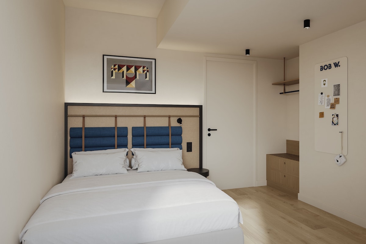 Un dormitorio con una cama, cabecero, una puerta y un cuadro colgado en la pared.