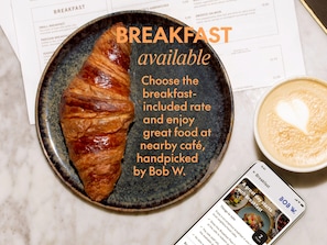 A croissant on a plate with a cup of coffee and a smartphone displaying a breakfast menu. - Bob W Athens Stadiou (Athina)