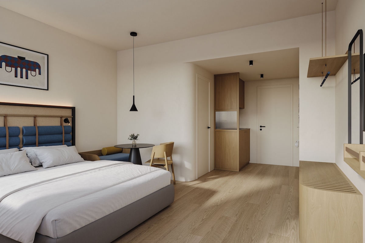 Habitación de hotel moderna con una cama grande, un escritorio, una silla, un televisor y una zona de cocina.