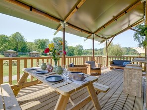 An outdoor wooden deck with a table set for dining, surrounded by wooden furniture and a covered area. - De Glamping - Sunny Trio | 14p by Interhome (Zeewolde)