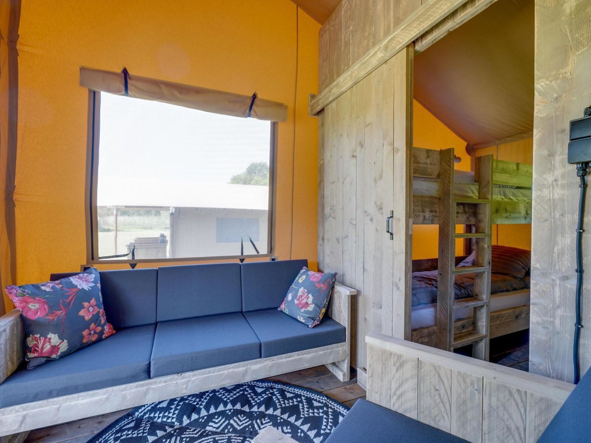 Ein Zimmer mit einer Couch, einem gemusterten Teppich, einem Fenster und einem Etagenbett.