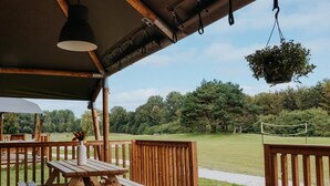 An outdoor wooden deck with picnic tables and hanging plants. - De Glamping - Trio Lodge | 18p by Interhome (Zeewolde)