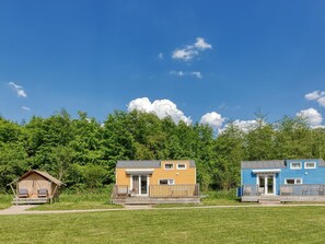A row of three cabins with a grassy foreground and a forested background. - De Glamping - Tiny Cinquette | 20p by Interhome (Zeewolde)