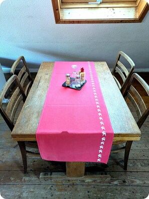Una mesa de comedor de madera con mantel rosa, rodeada de sillas de madera, y una ventana arriba.