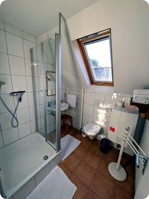 Un baño moderno con cabina de ducha de vidrio, un lavamanos blanco, un inodoro y una ventana con vistas.