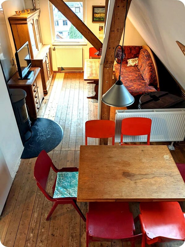 Un acogedor cuarto en el ático con una mesa de madera, sillas rojas, un sofá y un ventanal grande.