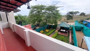 A balcony with a view of a garden area, including a bench and a small structure. - Silent Wild Cottages (Samudrapur)