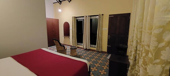 A hotel room with a bed, a chair, a small table, a wardrobe, and a door. - Silent Wild Cottages (Samudrapur)