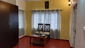 Una habitación con un armario de madera, una pequeña mesa con sillas y una cortina.