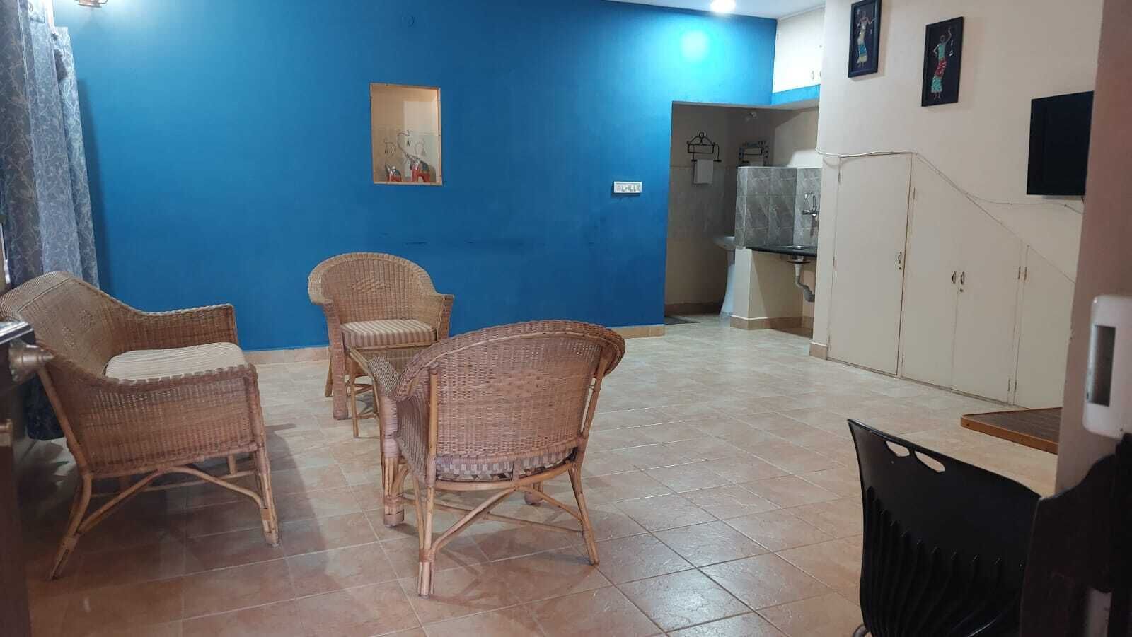A room with blue walls, wicker furniture, a tiled floor, and a kitchenette area.