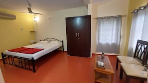 Een kamer met een bed, een houten stoel, een klein tafeltje, een kledingkast en een raam met gordijnen.