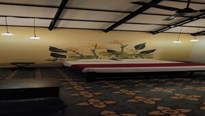 Habitación de hotel con cama, una mesita y un banco. Hay un ventilador de techo y luces colgantes.
