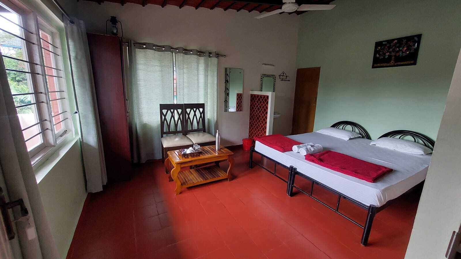 A room with a bed, a wooden table, a chair, and a window with curtains.