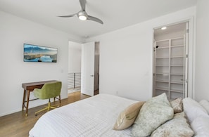 A bedroom with a bed, a desk, a chair, a ceiling fan, and a wardrobe.