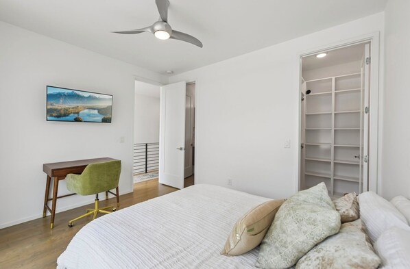A bedroom with a bed, a desk, a chair, a ceiling fan, and a wardrobe.