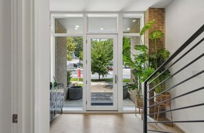 A hallway with a glass door leading to an outdoor area, a staircase, and a potted plant.