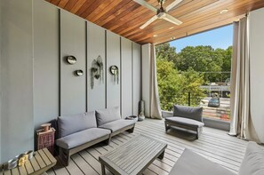 A modern balcony with a wooden ceiling, grey sofas, a small table, and a view of a cityscape.