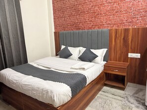 A neatly made bed with a grey and white duvet, a wooden headboard, and a nightstand with a drawer. - Janki Homestay Rishikesh Laxman Jhula (Rishikesh)