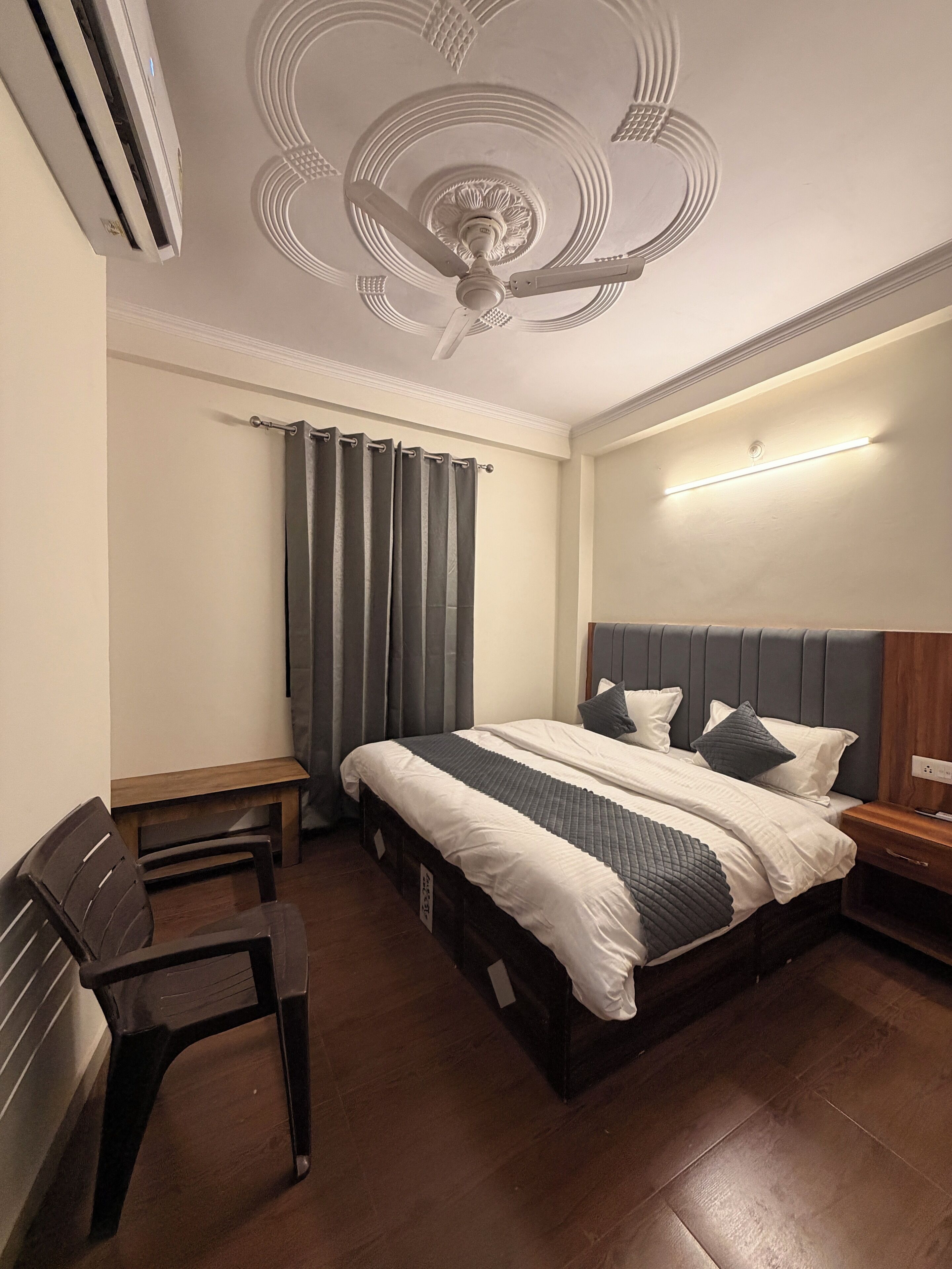 A bedroom with a bed, a desk, a chair, a ceiling fan, and a wall-mounted light.