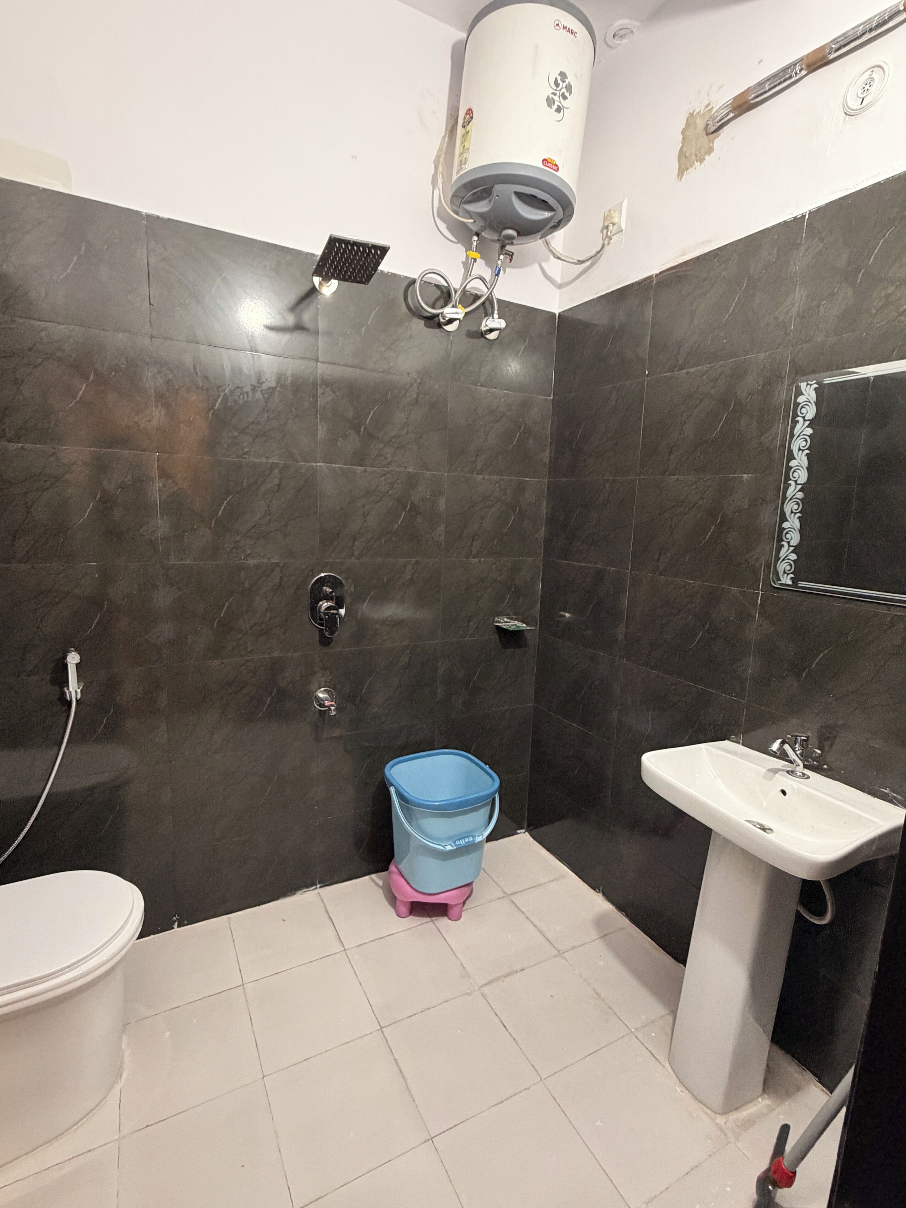 Un baño con inodoro, lavamanos, ducha y calentador de agua instalado en la pared.