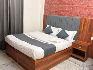 Una cama con estructura de madera, cabecera gris y ropa de cama blanca.