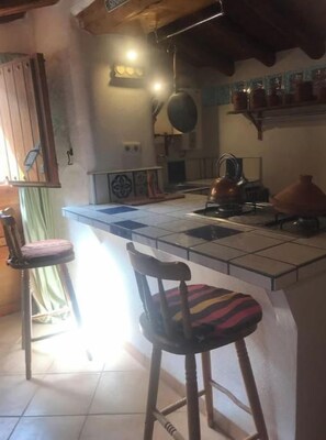 A kitchen with a central island, bar stools, a hanging pot rack, and a window with curtains.