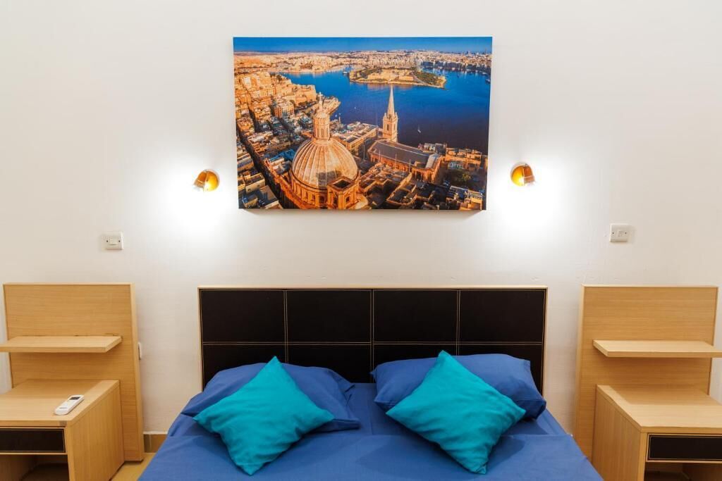 A hotel room with a bed, two bedside tables, and a wall-mounted painting of a cityscape.