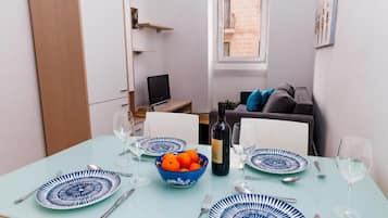 A dining area with a table set for four, a bowl of oranges, a bottle of wine, and a television in the background.