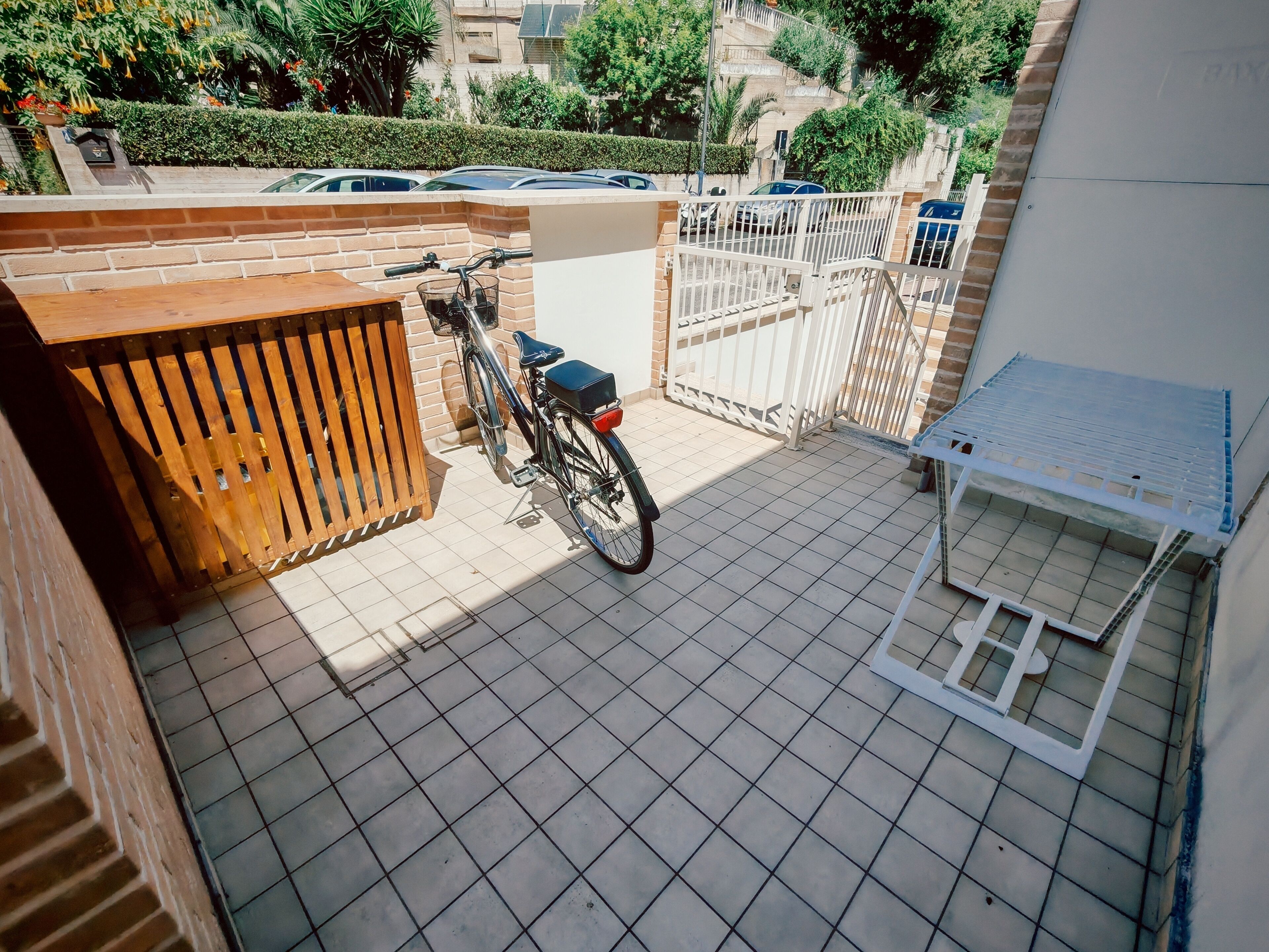 A tiled balcony with a bicycle, a wooden gate, and a white metal gate.