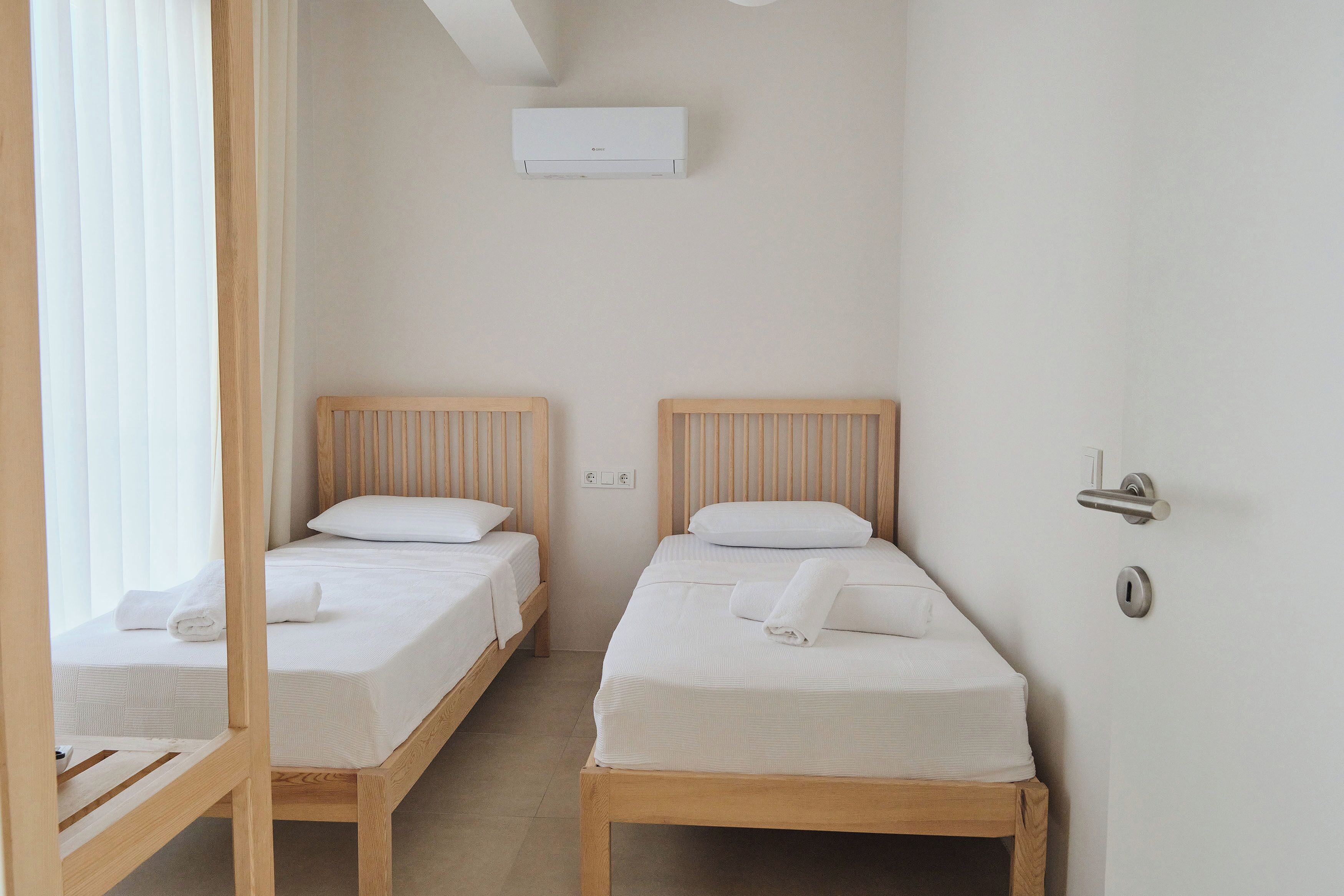Une chambre avec deux lits en bois, du linge de lit blanc et un appareil de climatisation fixé au mur.