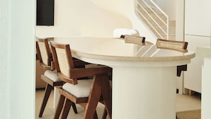 Uma área de refeições moderna com uma mesa redonda, cadeiras de madeira e uma parede branca.