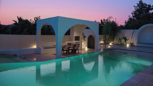 Piscina com área de estar coberta e pôr do sol ao fundo.