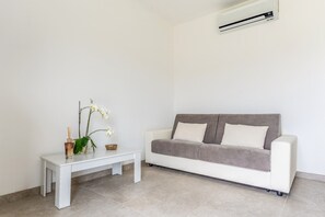 A minimalist living room with a white sofa, a small white table, and a potted orchid. - Casa Sale: Ocean-View Apartment in Taggia with Heated Hot Tub (Arma di Taggia)
