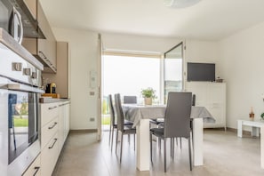 A modern kitchen with a dining area, a large window, and a flat-screen TV. - Casa Sale: Ocean-View Apartment in Taggia with Heated Hot Tub (Arma di Taggia)