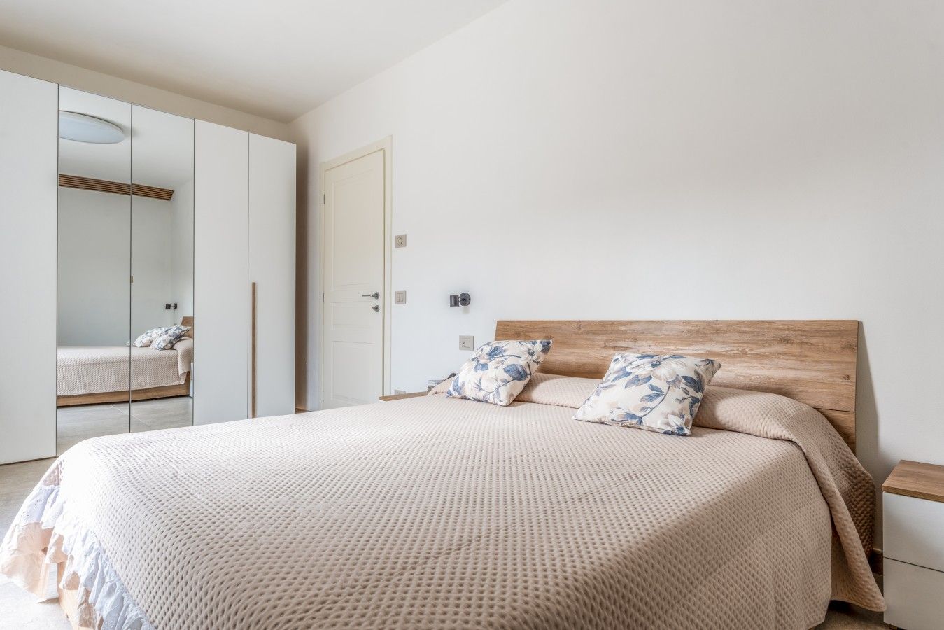 A bedroom with a bed, a wooden headboard, a wardrobe, and a mirror.