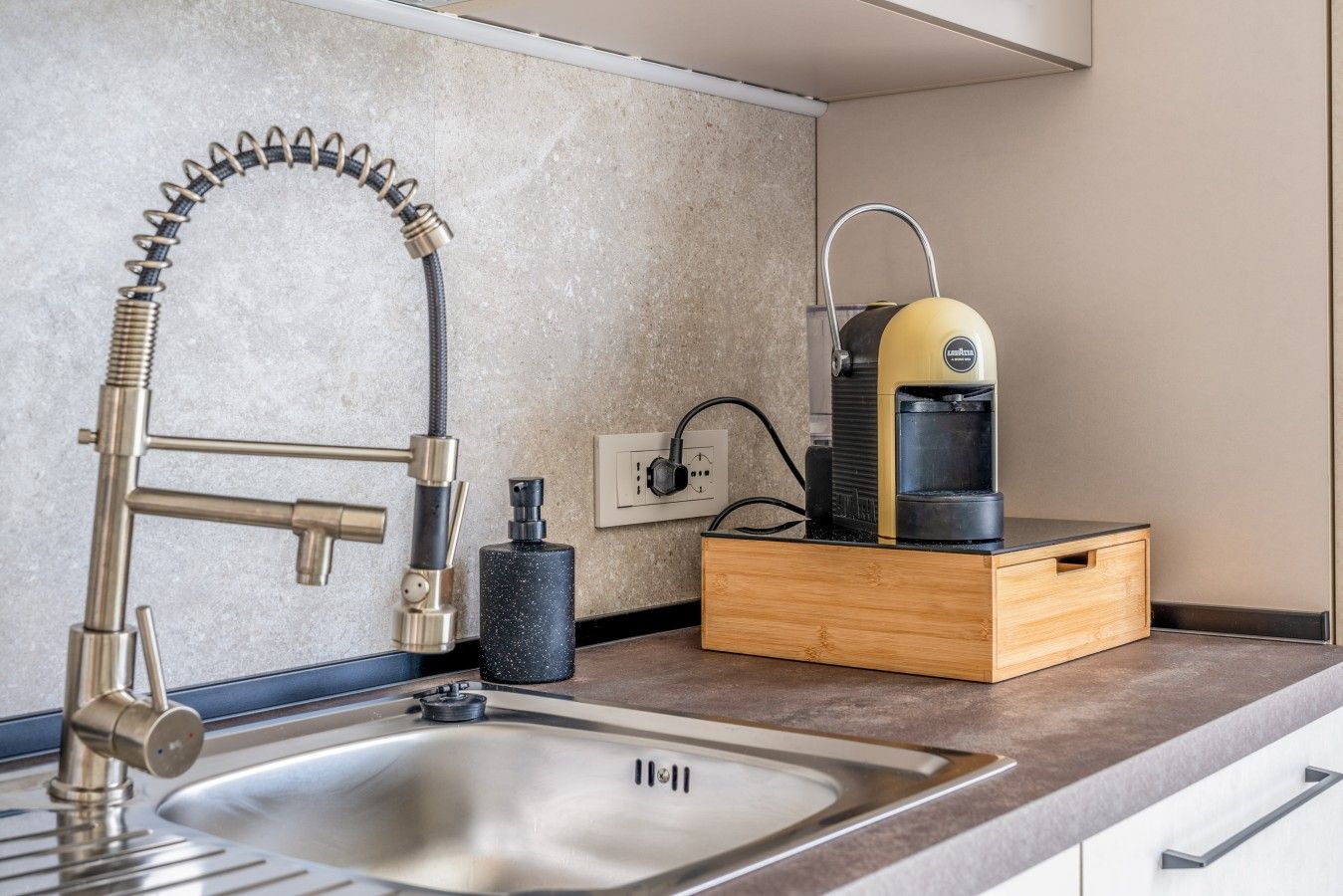 A kitchen with a modern faucet, a coffee maker, and a wooden box.