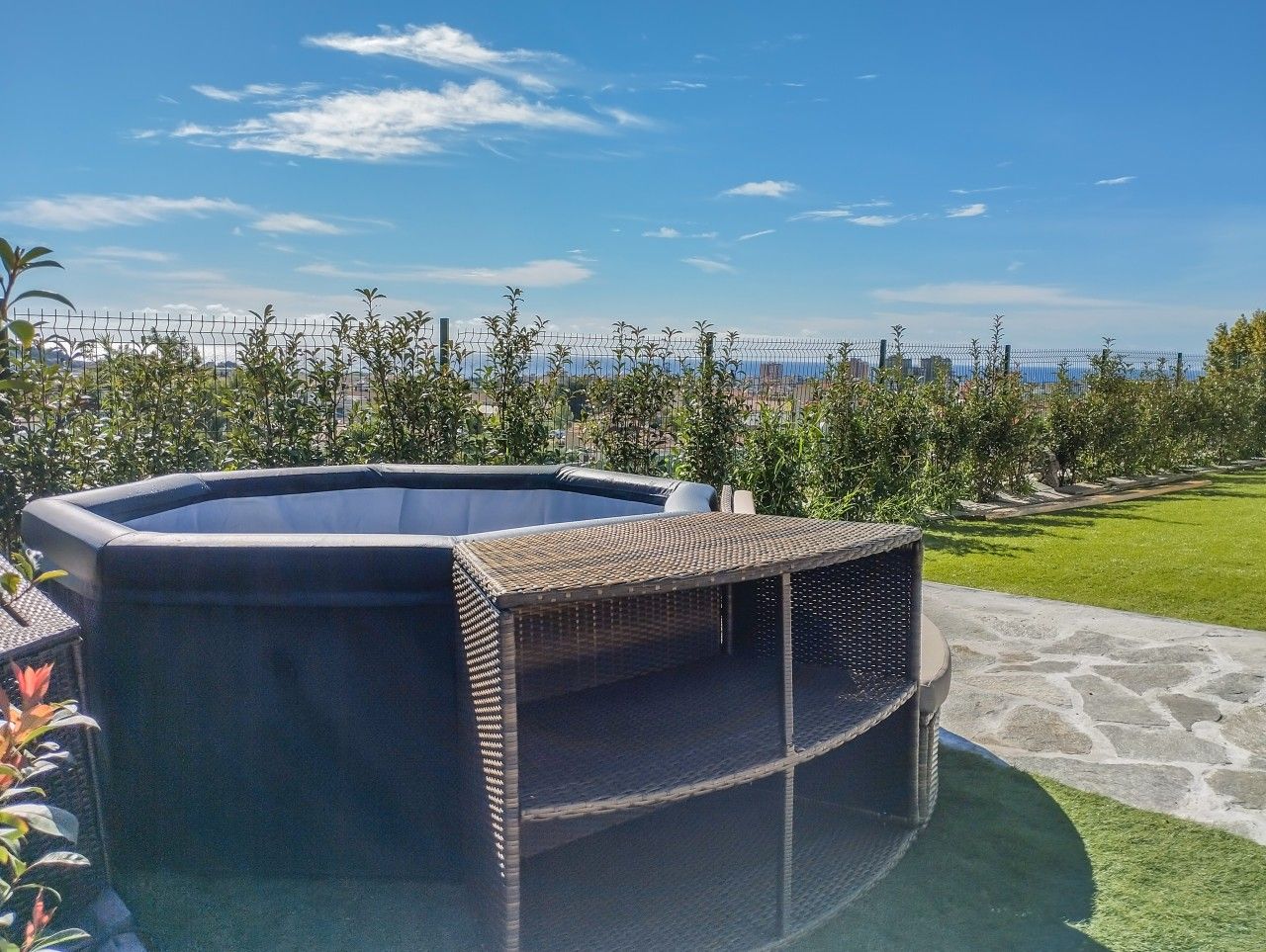 Un bain à remous entouré d’une structure en osier, lui-même bordé d’une terrasse en pierre et d’une pelouse.