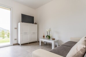 A modern living room with a sofa, a television on a cabinet, a small table with a vase of flowers, and a sliding glass door leading to a balcony. - Casa Sale: Apartment with an ocean view in Taggia featuring a heated hot tub (Arma di Taggia)
