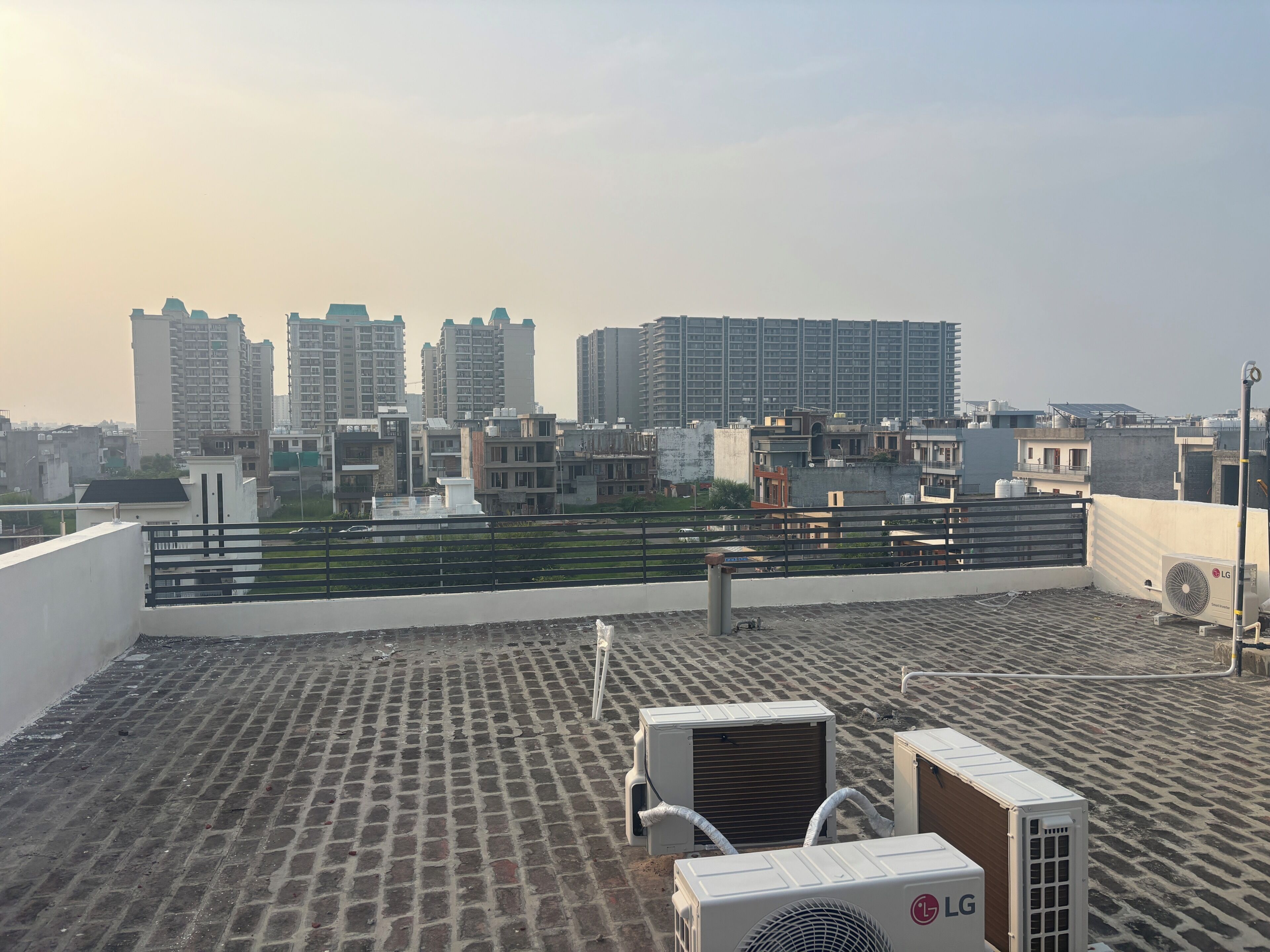 Eine Dachterrasse mit Klimaanlagen, einem Metallgeländer und Blick auf eine Skyline mit Hochhäusern.