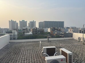 A rooftop with air conditioning units, a metal railing, and a view of a cityscape with high-rise buildings. - Beautiful 3-BHK  with Balcony in Sahibzada Ajit Singh Nagar Chandigarh Airport (Sahibzada Ajit Singh Nagar)