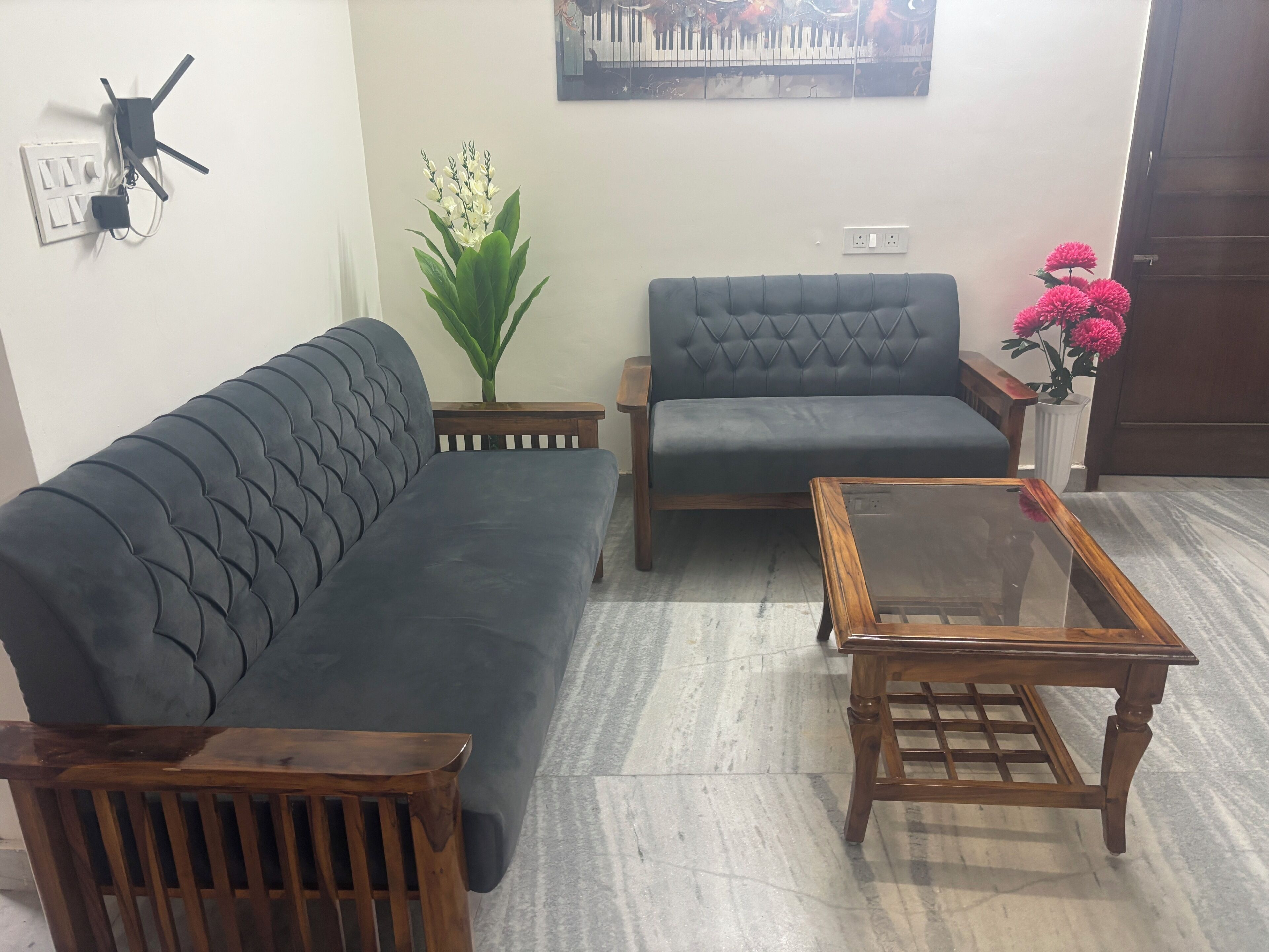 Ein Wohnzimmer mit einem dunkelgrauen Sofa, einem Holztisch und einer Topfpflanze.