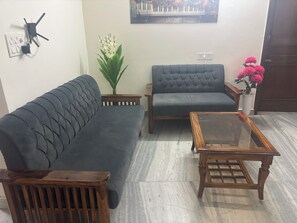 A living room with a dark grey sofa, a wooden coffee table, and a potted plant. - Beautiful 3-BHK with Balcony in Sahibzada Ajit Singh Nagar Chandigarh Airport (Sahibzada Ajit Singh Nagar)