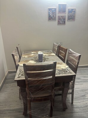A dining table with six chairs, some wrapped in plastic, and a small box on the table. - Beautiful 3-BHK with Balcony in Sahibzada Ajit Singh Nagar Chandigarh Airport (Sahibzada Ajit Singh Nagar)
