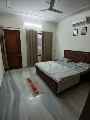 A bedroom with a bed, a ceiling fan, an air conditioner, and a view through a window. - Beautiful 3-BHK with Balcony in Sahibzada Ajit Singh Nagar Chandigarh Airport (Sahibzada Ajit Singh Nagar)