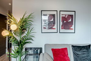 Una sala de estar moderna con un sofá, dos cuadros abstractos enmarcados, una planta grande en maceta y una lámpara de pie.
