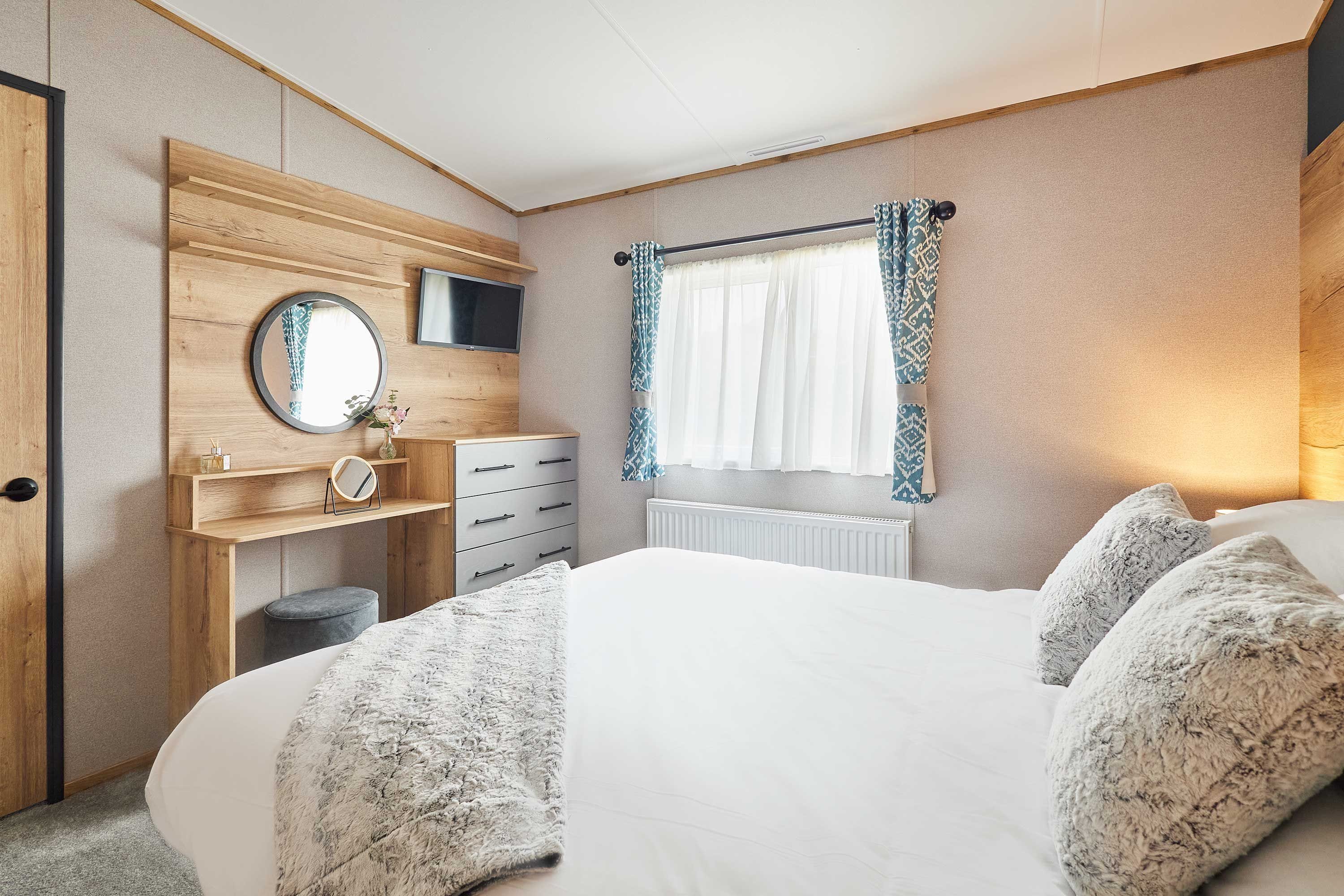 A bedroom with a bed, a dresser, a mirror, a television, and a window with curtains.